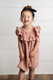 Child wearing a pink dress with ruffles against a white wall