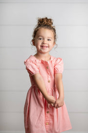 Young girl wearing a pink dress with buttons on a plain background